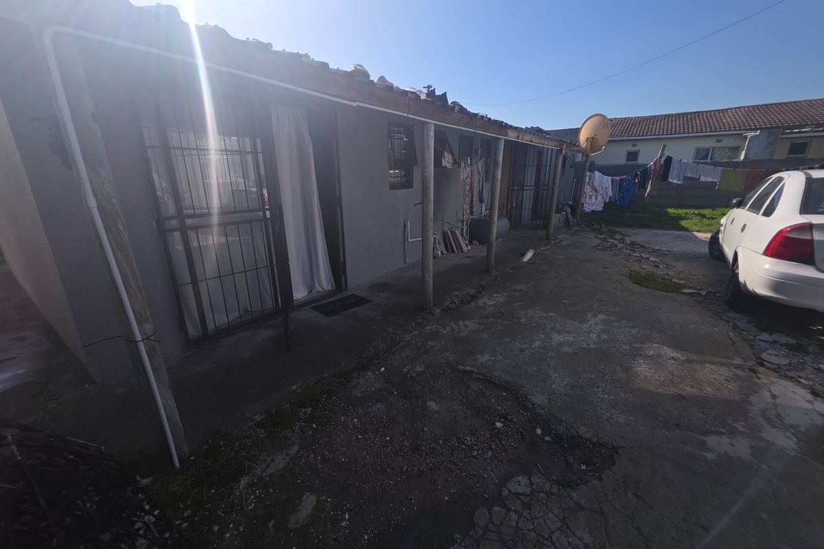 Rear exterior view of the property featuring a concrete patio area, security gates, and roof structure requiring maintenance.