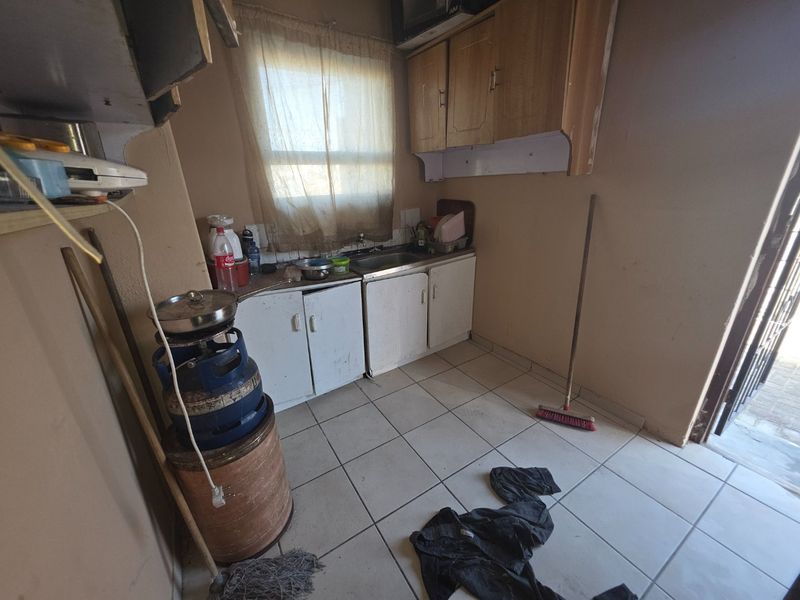 A small, dated kitchen area featuring basic built-in cabinetry, a stainless steel sink, and tiled flooring, requiring significant cosmetic updates.