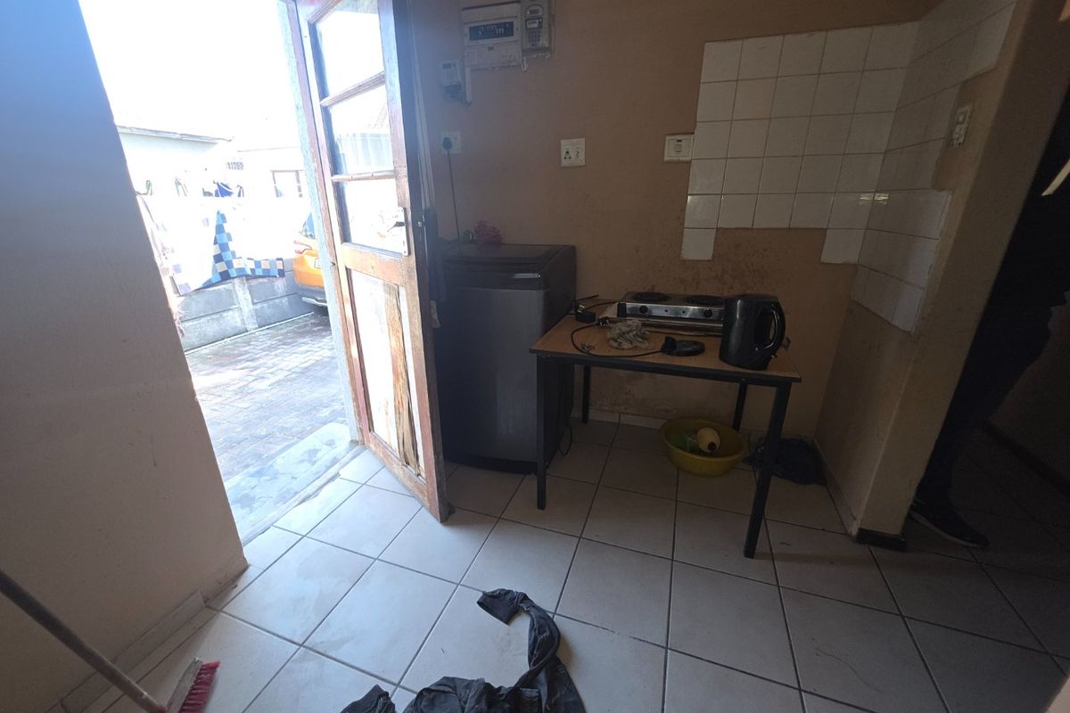 A small kitchen area featuring tiled flooring, a tiled splashback, and a wall-mounted electrical distribution board, requiring significant cosmetic renovation and wall repairs.