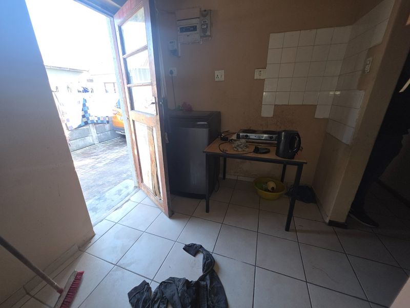A small kitchen area featuring tiled flooring, a tiled splashback, and a wall-mounted electrical distribution board, requiring significant cosmetic renovation and wall repairs.