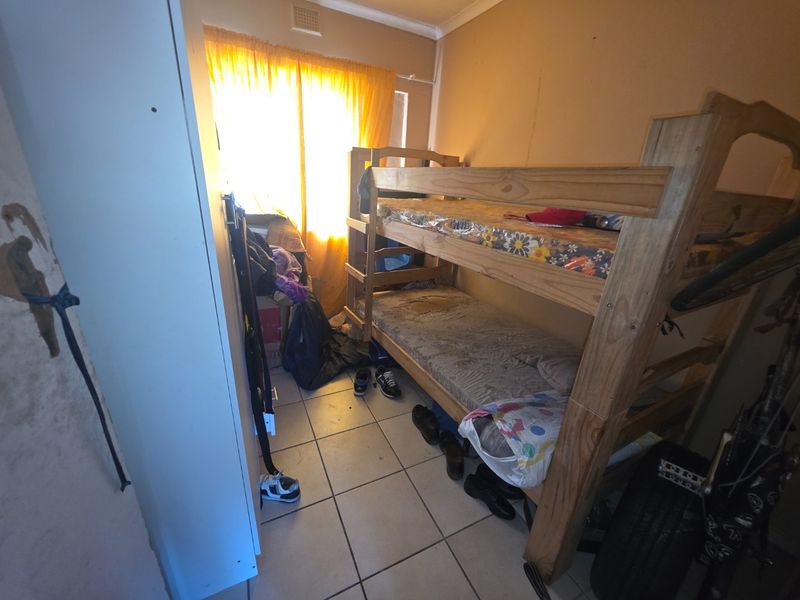 A bedroom featuring tiled flooring and a built-in cupboard, currently showing signs of wear and requiring cosmetic updates to the wall finishes.