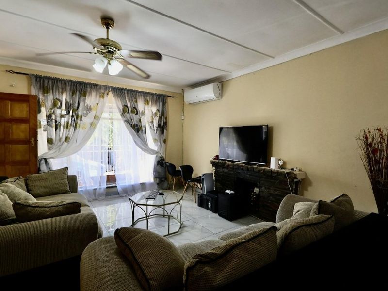 A comfortable living room featuring tiled flooring, a stone-clad feature wall, a ceiling fan, and a wall-mounted air conditioning unit.