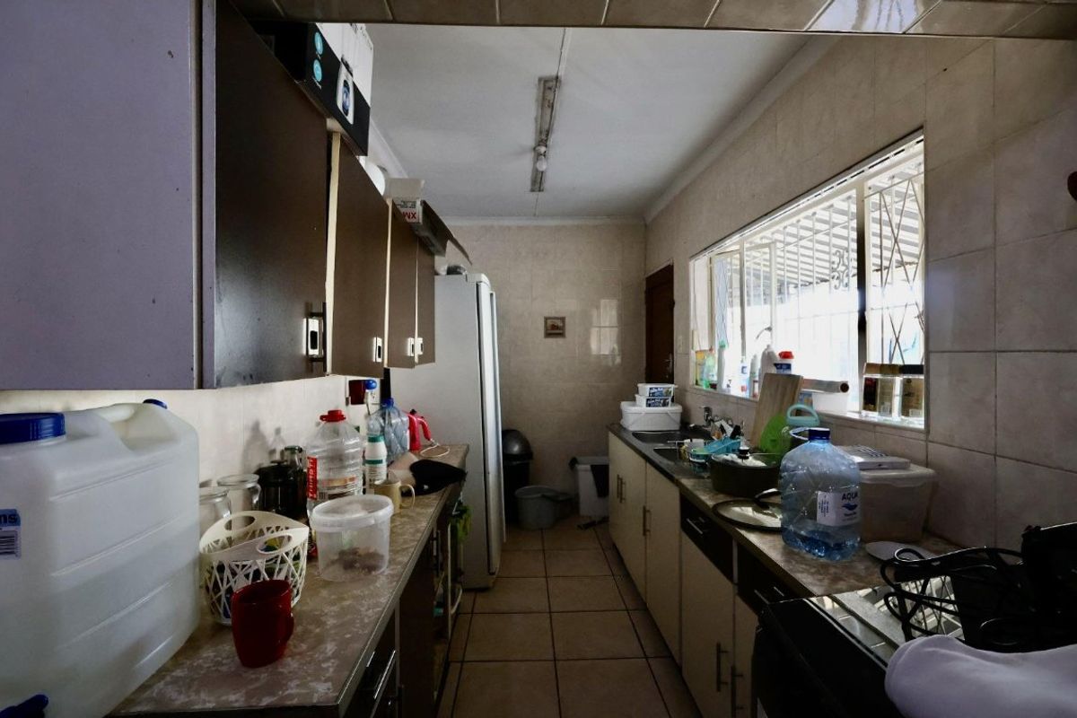 A functional kitchen featuring tiled walls and flooring, built-in cabinetry, and a double sink with security bars on the windows.