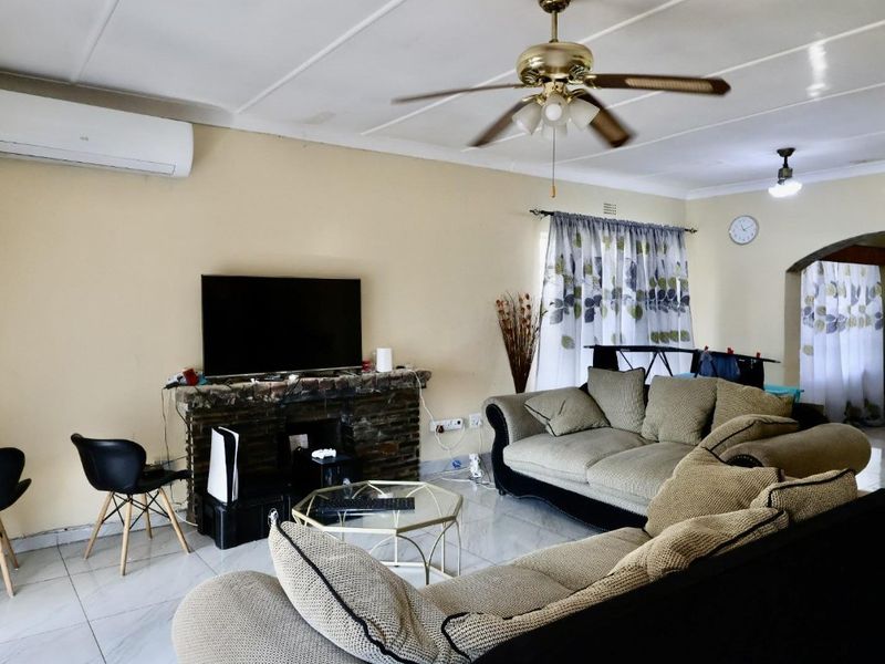 A spacious living room featuring tiled flooring, a stone fireplace, a ceiling fan, and a wall-mounted air conditioning unit.