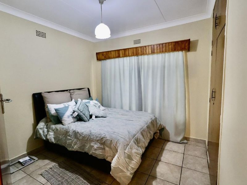 A functional bedroom featuring tiled flooring, built-in cupboards, and a timber pelmet detail above the window area.