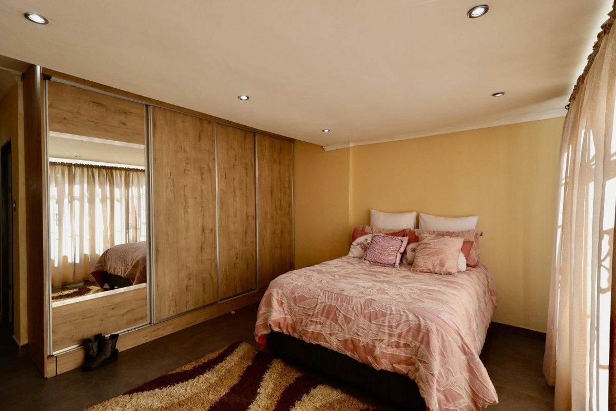 A well-maintained bedroom featuring built-in wooden wardrobes with mirrored panels, recessed downlighting, and tiled flooring.