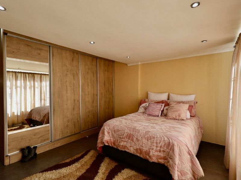 A well-maintained bedroom featuring built-in wooden wardrobes with mirrored panels, recessed downlighting, and tiled flooring.