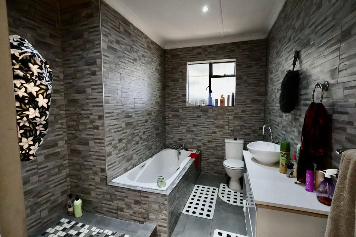 A modern bathroom featuring full-height textured stone-look wall tiles, a built-in bathtub, a vessel sink vanity, and a toilet.