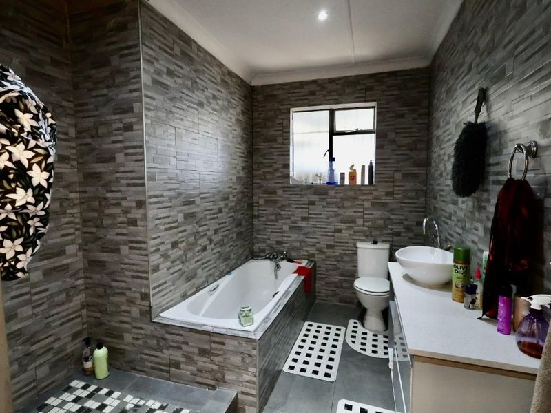 A modern bathroom featuring full-height textured stone-look wall tiles, a built-in bathtub, a vessel sink vanity, and a toilet.