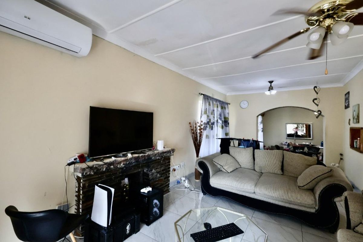 A living room featuring a brick fireplace, tiled flooring, ceiling fan, and split-system air conditioning, with an arched opening leading to an adjacent space.