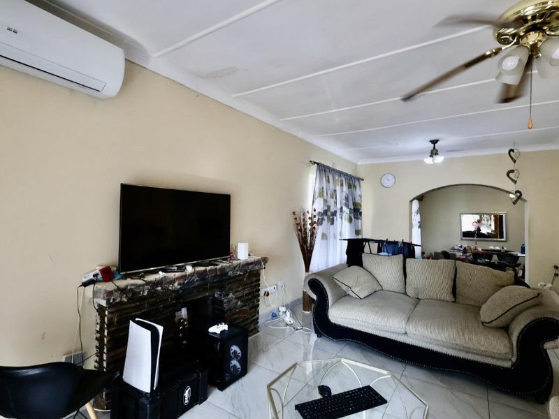 A living room featuring a brick fireplace, tiled flooring, ceiling fan, and split-system air conditioning, with an arched opening leading to an adjacent space.