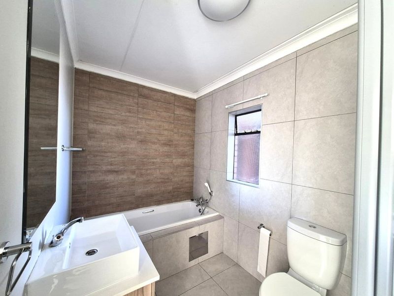 A modern, well-maintained bathroom featuring a bathtub, contemporary basin, toilet, and neutral-toned wall and floor tiling.