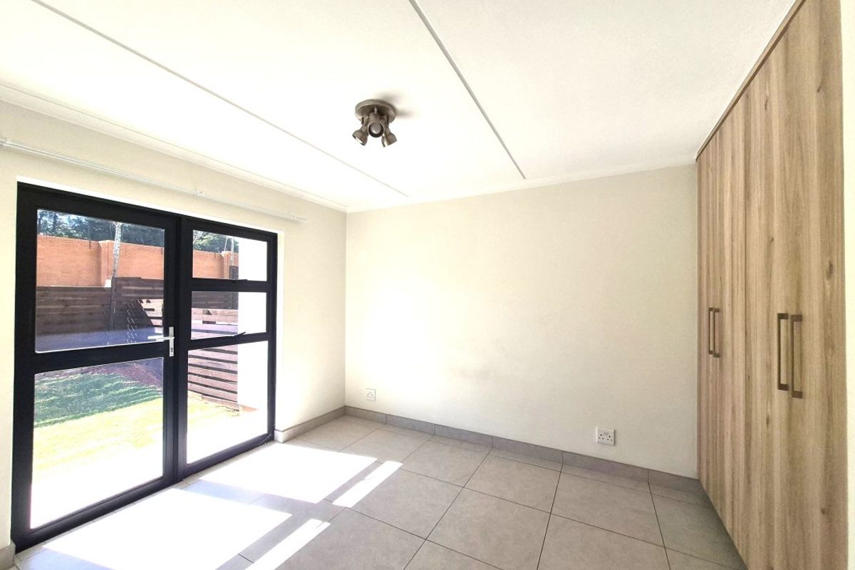 A bright, empty bedroom featuring modern tiled flooring, built-in wooden cupboards, and a glass door providing direct access to the outdoor area.