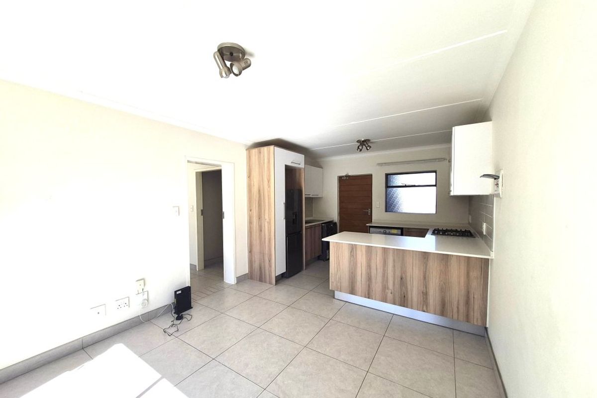 Modern open-plan kitchen featuring wood-look cabinetry, stone countertops, a gas hob, and neutral tiled flooring, offering a clean and functional living space.