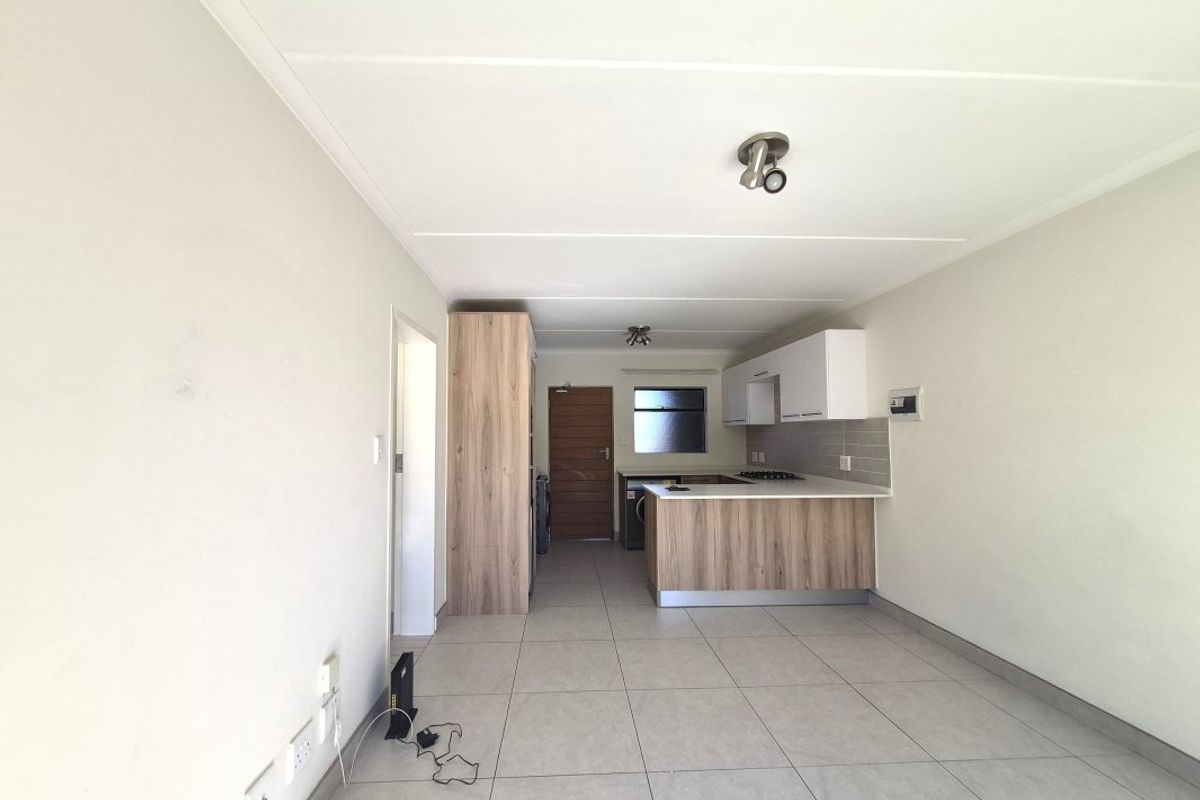 An open-plan living and kitchen area featuring modern wood-finish cabinetry, a kitchen island with a gas hob, and neutral tiled flooring throughout.