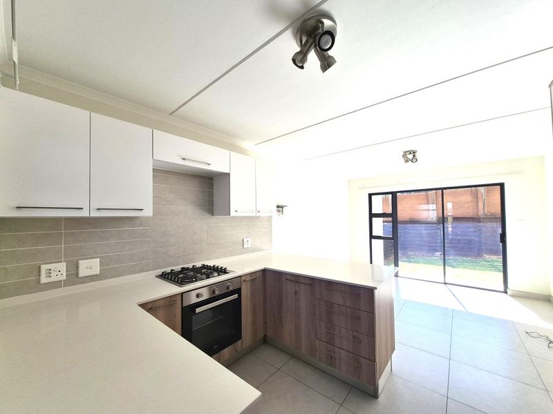 Modern open-plan kitchen featuring stone countertops, gas hob, built-in oven, and sleek cabinetry, flowing seamlessly into a bright living area with sliding door access.