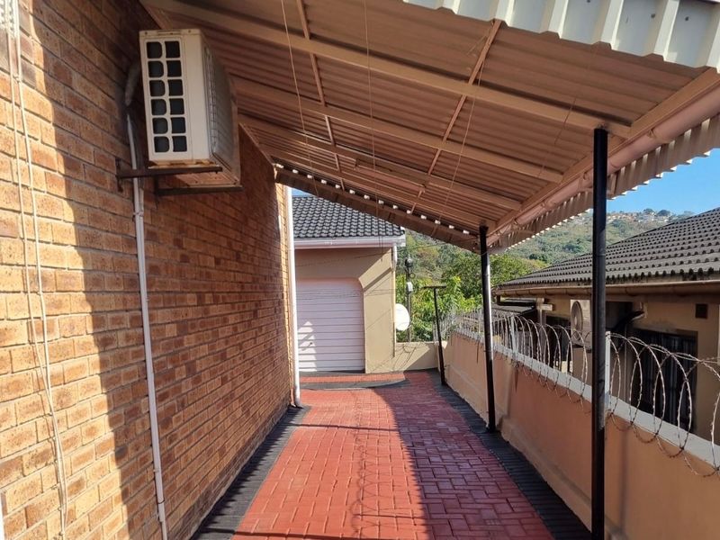 A covered outdoor walkway featuring brick paving, metal roofing, and security fencing, providing access along the side of the property.