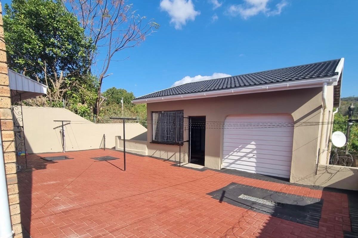Rear exterior view featuring a paved courtyard area, garage access, and secure boundary walls under a clear sky.