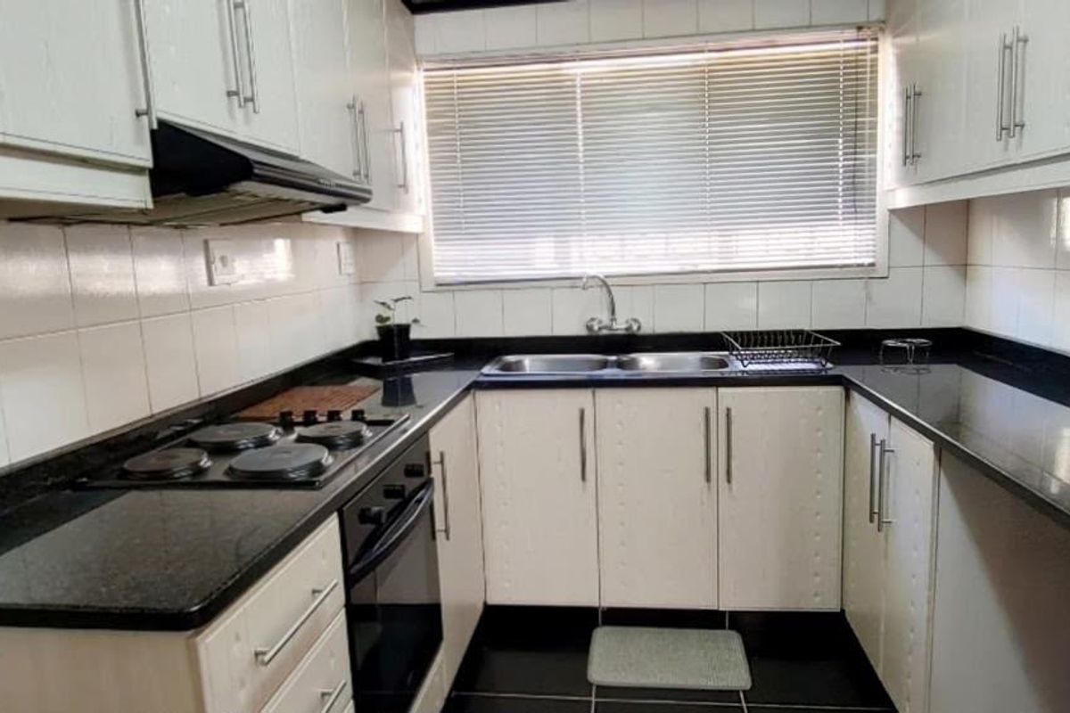 A functional U-shaped kitchen featuring white cabinetry, dark granite countertops, a built-in electric hob, oven, and a double bowl sink with tiled backsplash.