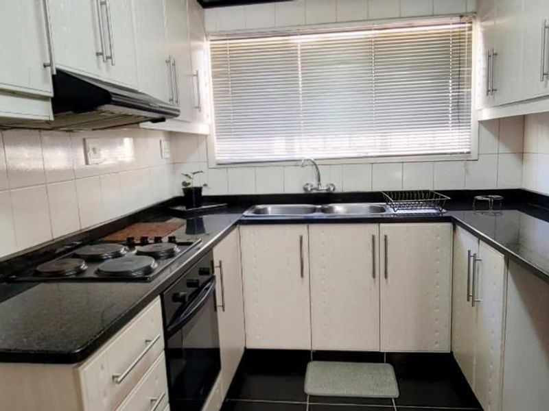A functional U-shaped kitchen featuring white cabinetry, dark granite countertops, a built-in electric hob, oven, and a double bowl sink with tiled backsplash.