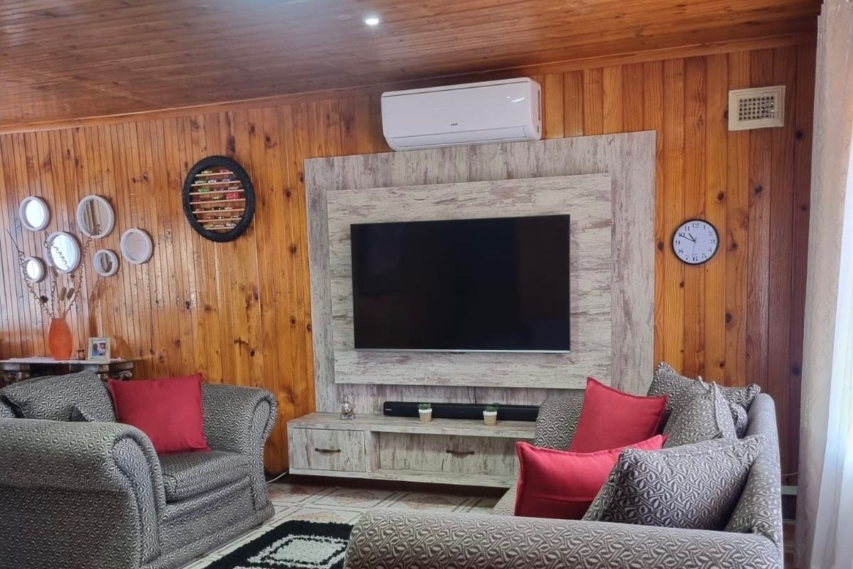 A cozy living room featuring warm timber wall paneling, a timber ceiling, and a modern built-in media console with an integrated split-system air conditioner.