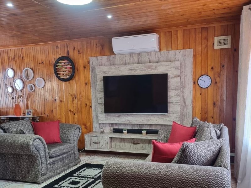 A cozy living room featuring warm timber wall paneling, a timber ceiling, and a modern built-in media console with an integrated split-system air conditioner.