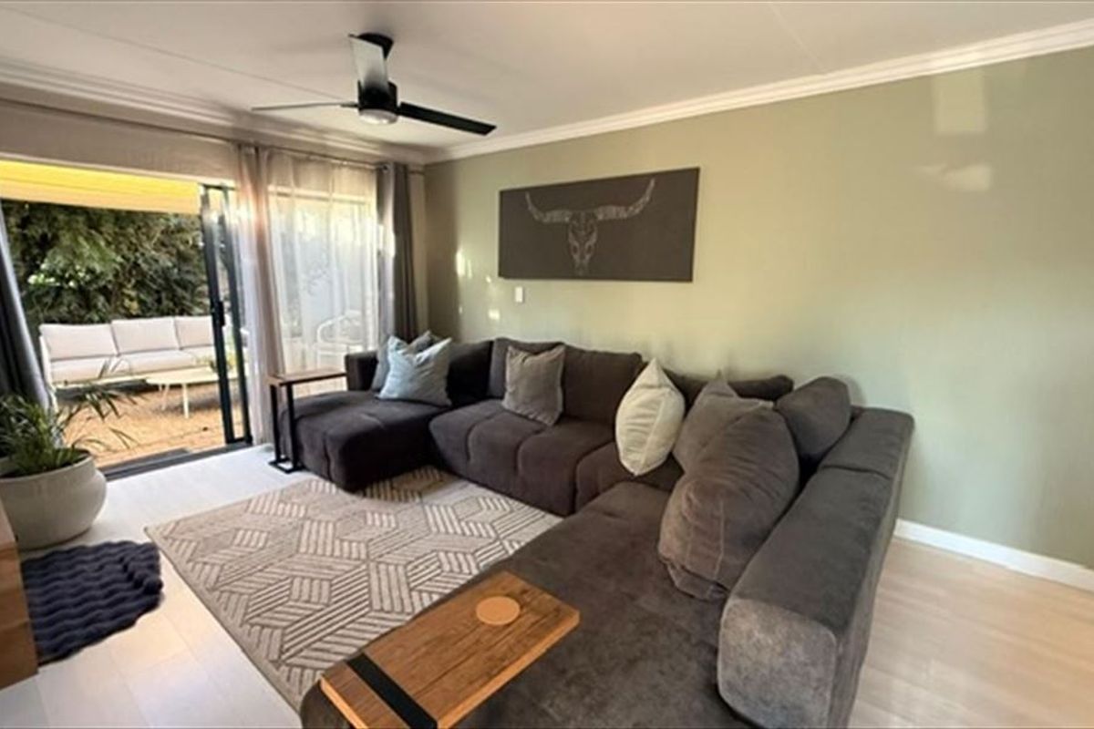 A well-maintained living room featuring light laminate flooring, crown molding, a modern ceiling fan, and large sliding glass doors leading to an outdoor patio.