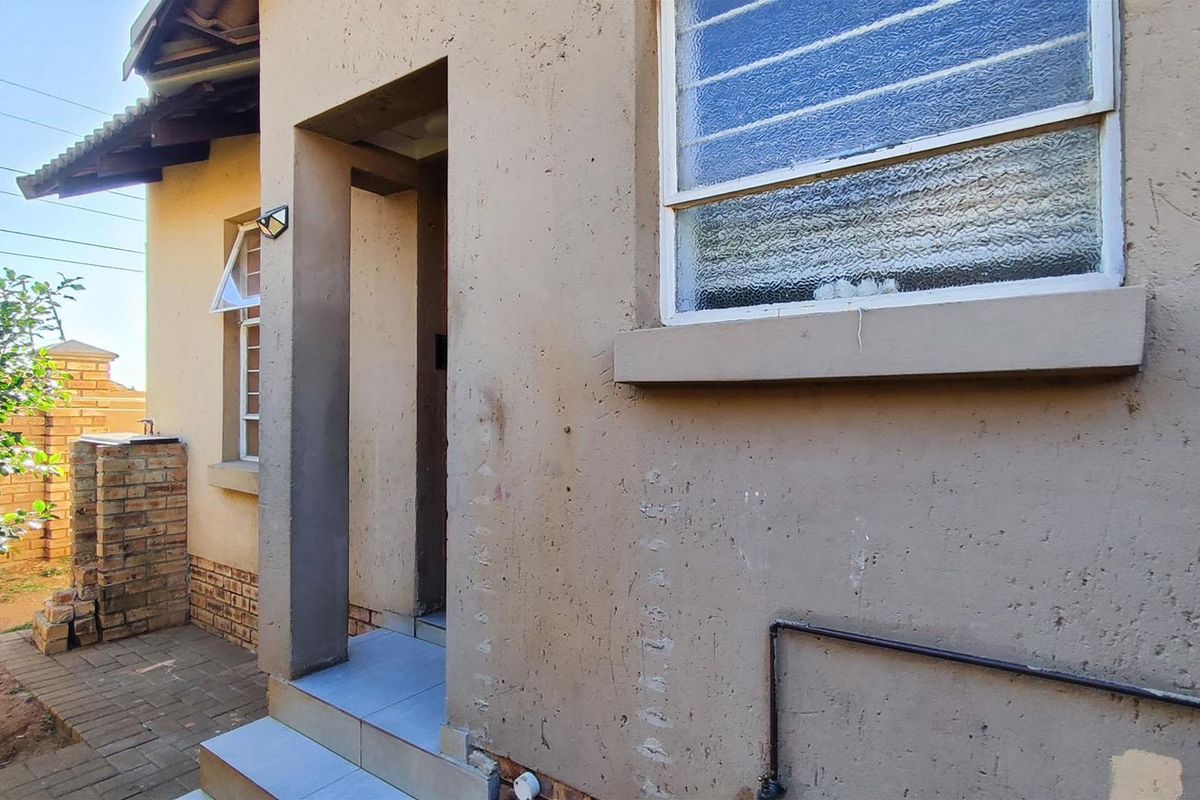 A view of the rear exterior of the townhouse, featuring a paved walkway, tiled entrance step, and security bars on the window.