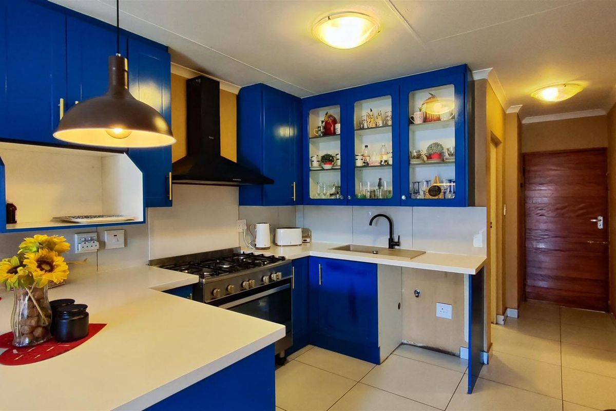A kitchen featuring vibrant blue cabinetry, a gas stove with extractor fan, and light-colored countertops, with an open space for an under-counter appliance.