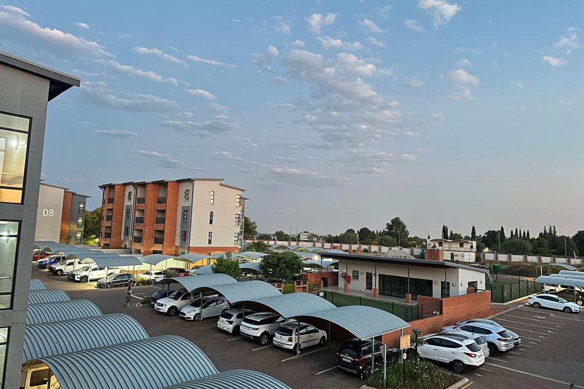 An elevated view of the apartment complex grounds, featuring extensive paved parking with covered carports and well-maintained brick building facades.