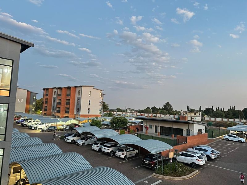 An elevated view of the apartment complex grounds, featuring extensive paved parking with covered carports and well-maintained brick building facades.