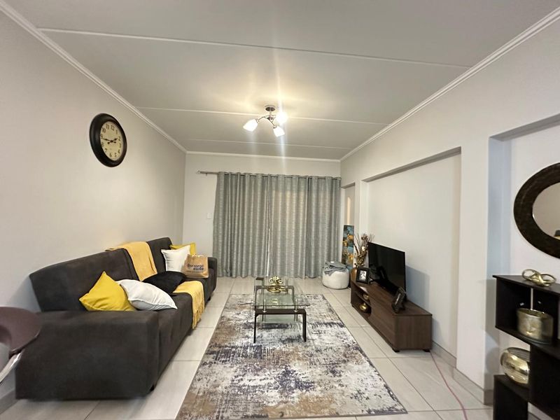 A well-maintained living room featuring neutral tiled flooring, ceiling coving, and a sliding door leading to an outdoor area.