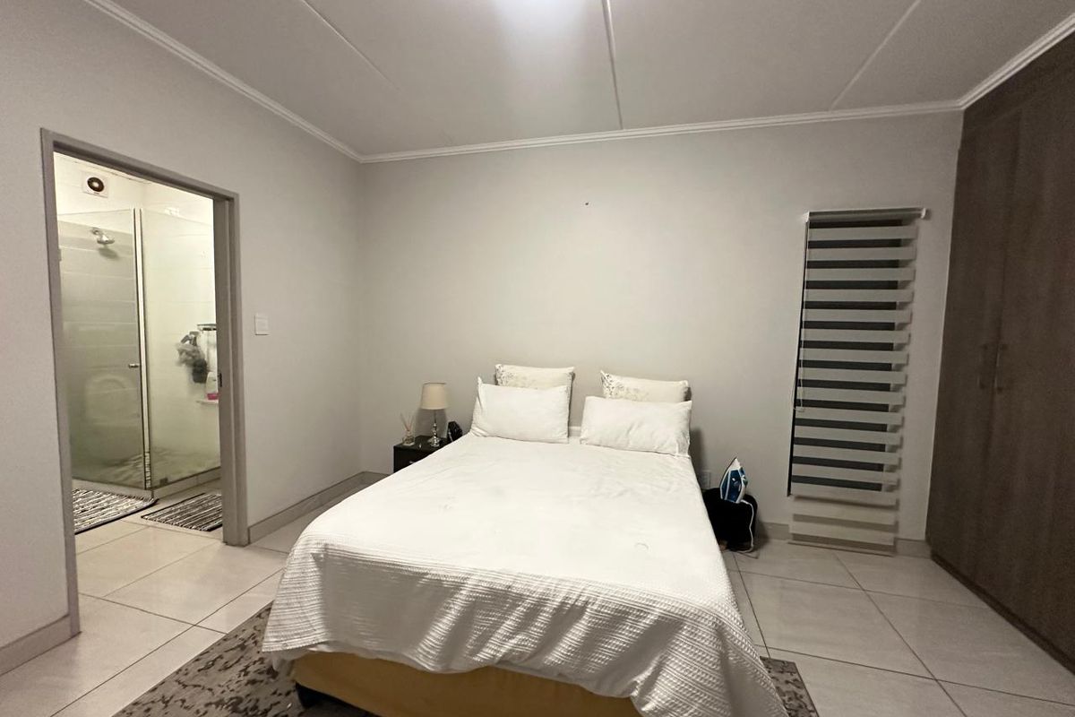 A well-maintained bedroom featuring tiled flooring, built-in cupboards, zebra blinds, and an attached en-suite bathroom.