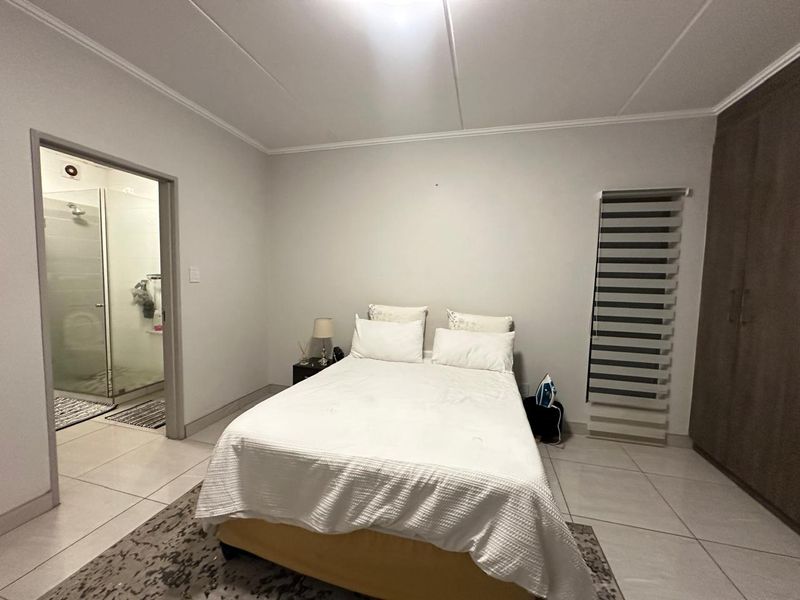 A well-maintained bedroom featuring tiled flooring, built-in cupboards, zebra blinds, and an attached en-suite bathroom.