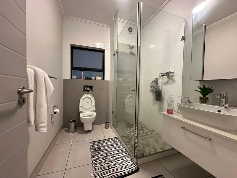 Modern bathroom featuring a glass-enclosed shower, wall-mounted vanity with vessel sink, and neutral tiled finishes throughout.