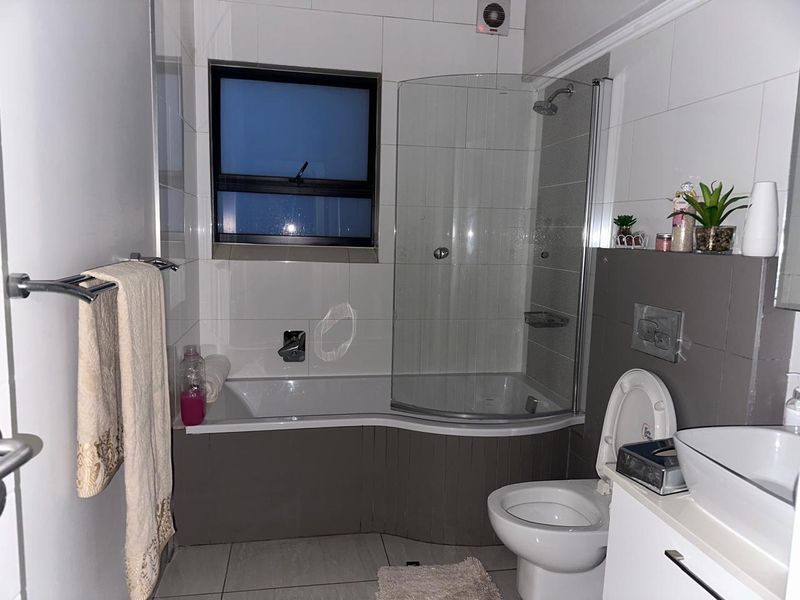 Modern bathroom featuring a shower-over-bath combination with a glass screen, wall-mounted toilet, and a contemporary vessel sink vanity unit.