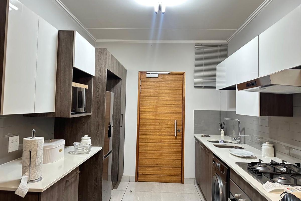 Modern galley-style kitchen featuring sleek two-tone cabinetry, stone countertops, integrated appliances, gas hob, and tiled flooring.