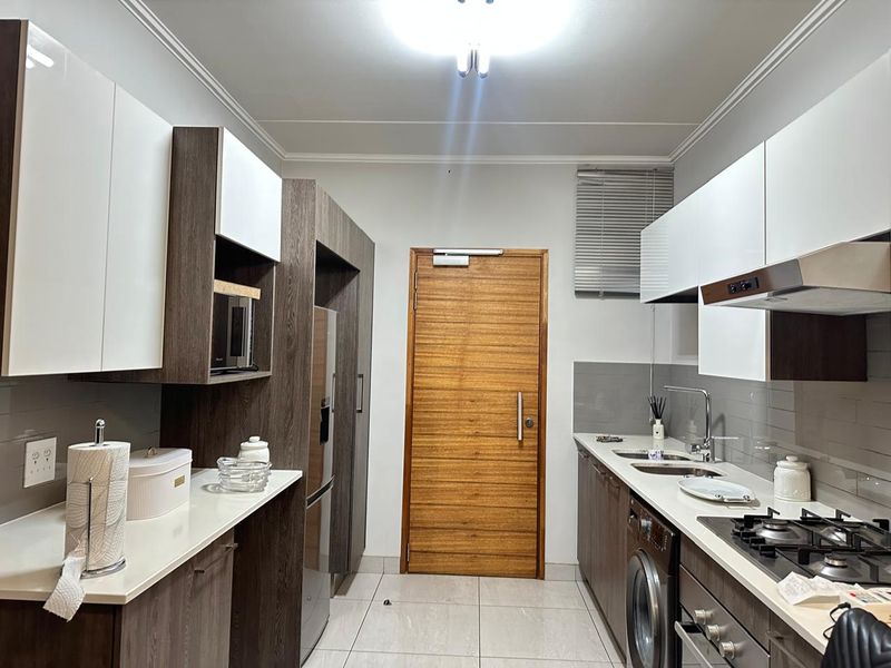 Modern galley-style kitchen featuring sleek two-tone cabinetry, stone countertops, integrated appliances, gas hob, and tiled flooring.