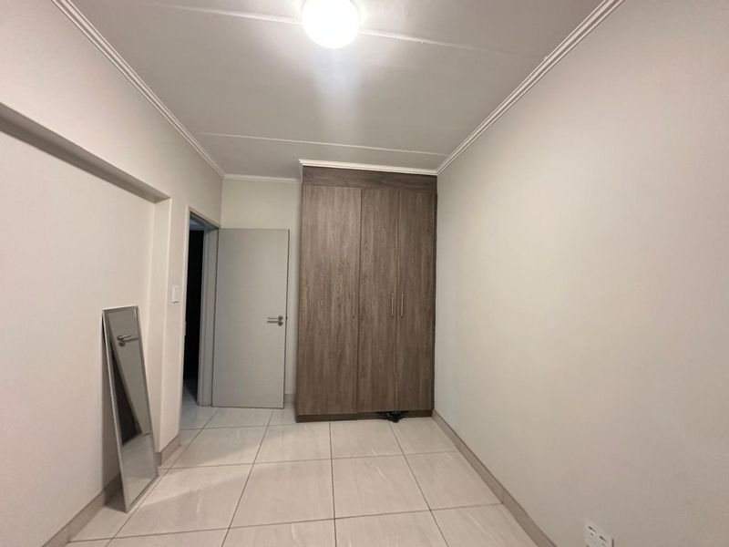 A clean, empty bedroom featuring neutral tiled flooring, a modern wood-finish built-in wardrobe, and simple ceiling lighting.