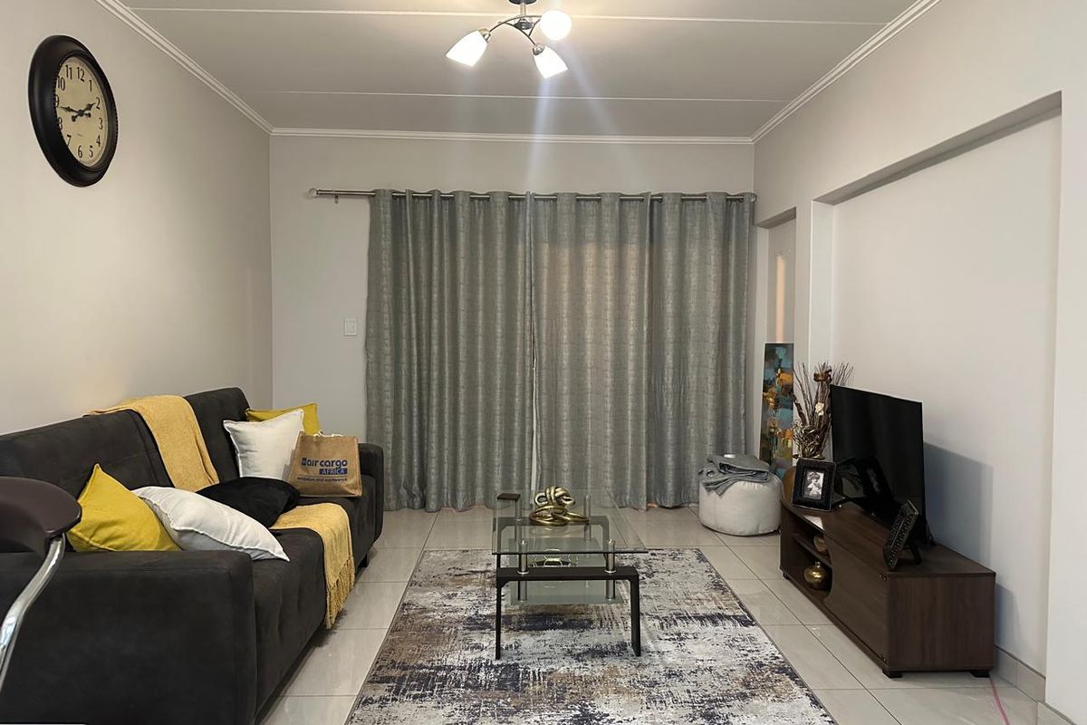 A well-maintained living room featuring neutral tiled flooring, ceiling cornicing, and full-length curtain tracks, providing a clean and functional space.