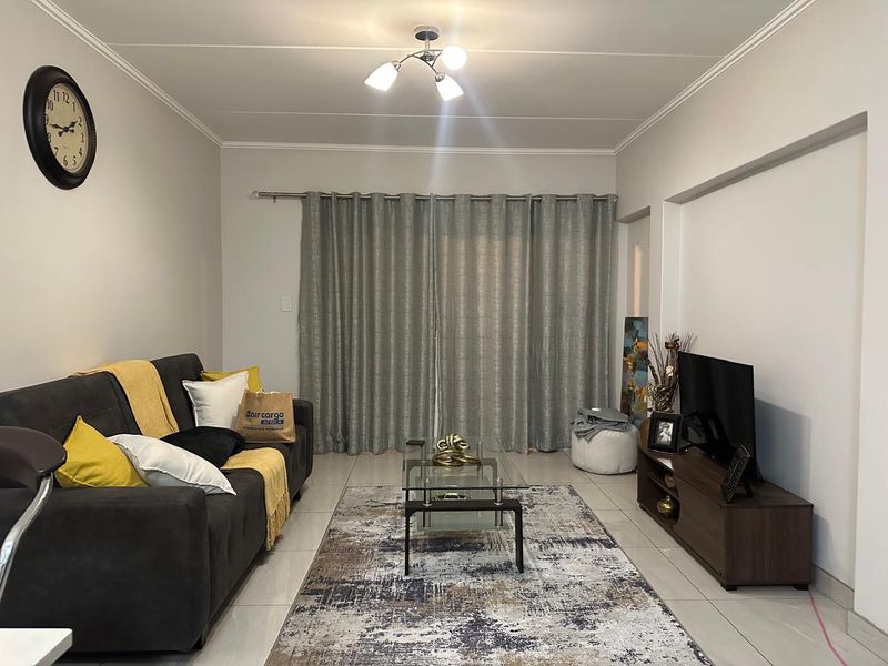 A well-maintained living room featuring neutral tiled flooring, ceiling cornicing, and full-length curtain tracks, providing a clean and functional space.