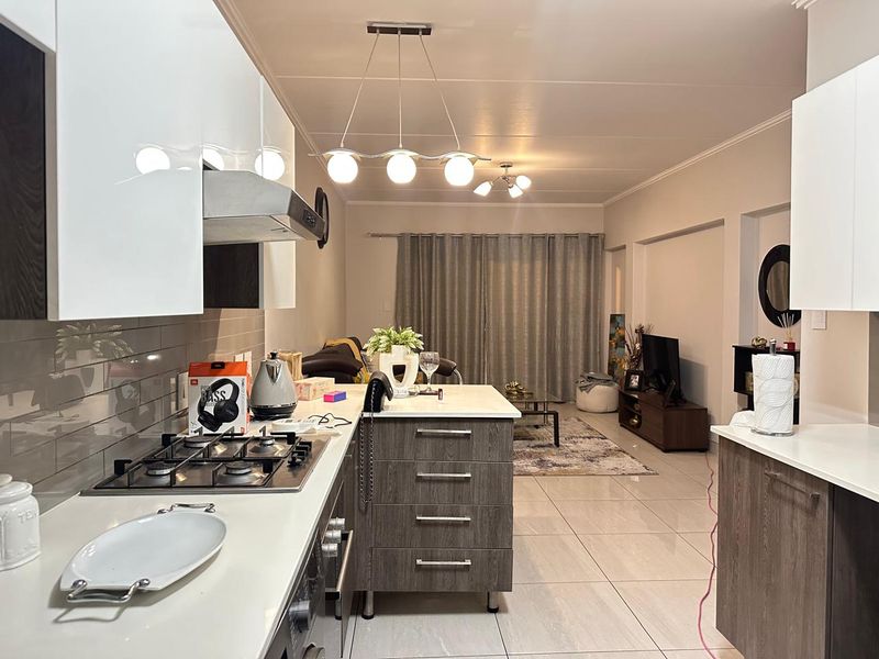 Modern open-plan kitchen and living area featuring a central island, gas hob, sleek cabinetry, and polished floor tiles throughout the space.