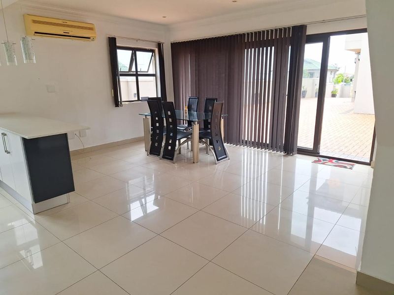 Spacious open-plan living and dining area featuring polished tiled floors, a kitchen island, and large sliding glass doors leading to an outdoor patio.