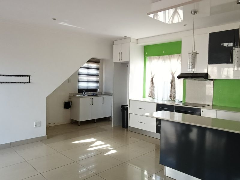 Spacious open-plan kitchen and living area featuring modern two-tone cabinetry, a central island, and tiled flooring throughout.