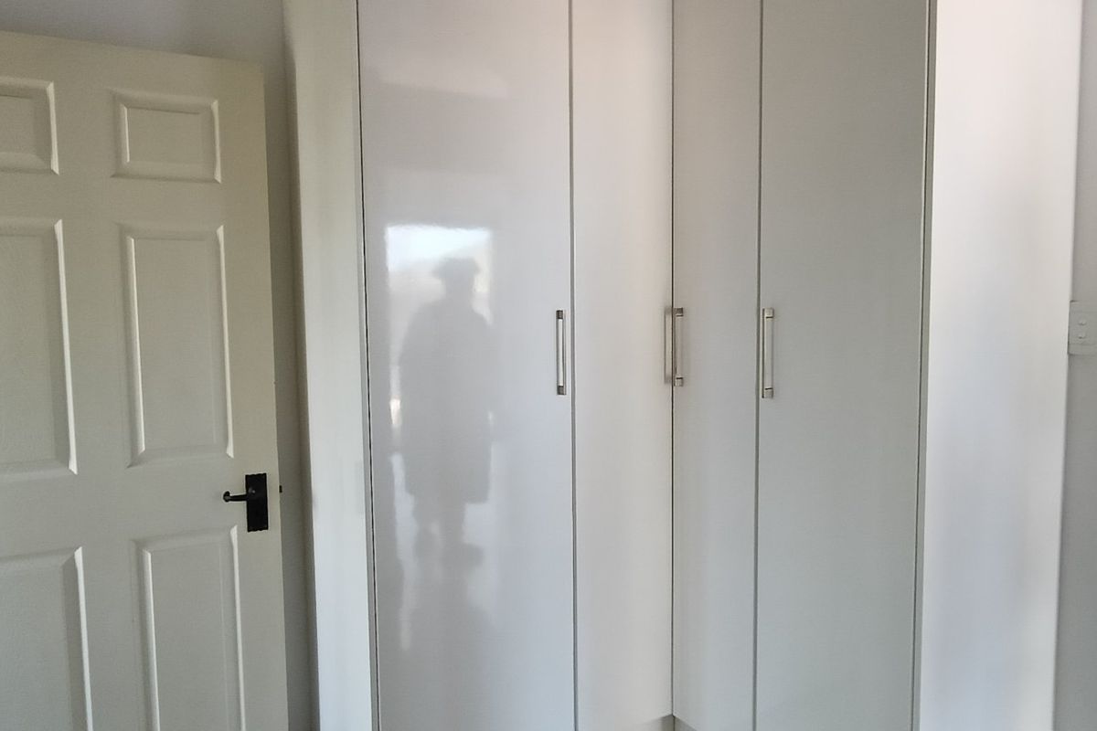 A clean bedroom interior featuring modern white built-in cupboards with sleek handles and a standard internal door.