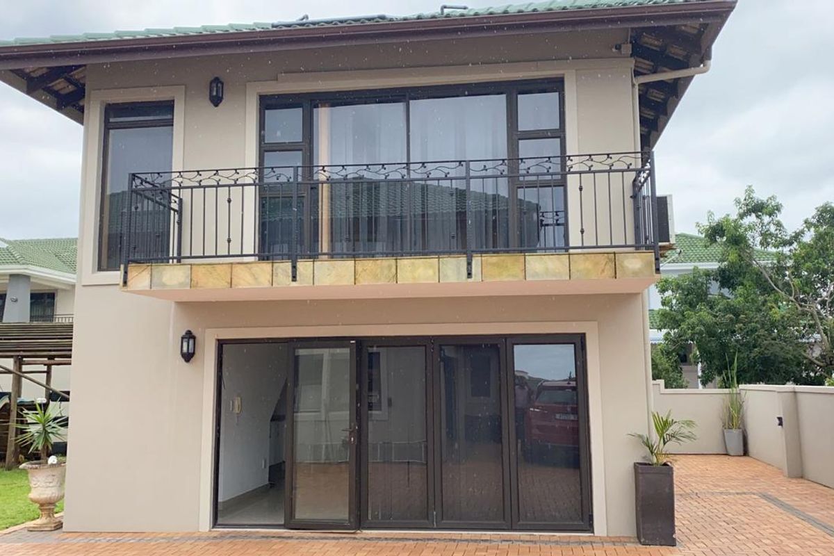 Rear view of a two-story apartment featuring a balcony with wrought iron railings, sliding glass doors, and a paved patio area.