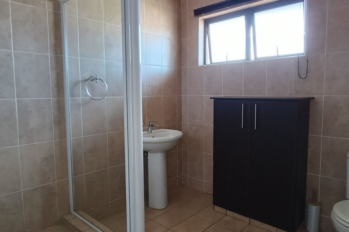 A functional bathroom featuring a shower enclosure, pedestal basin, toilet, and tiled finishes throughout, providing a clean and practical space.