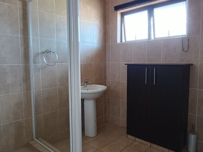 A functional bathroom featuring a shower enclosure, pedestal basin, toilet, and tiled finishes throughout, providing a clean and practical space.