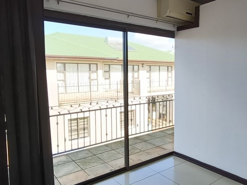An empty living area featuring tiled flooring, a wall-mounted air conditioning unit, and large sliding glass doors opening onto a private balcony.