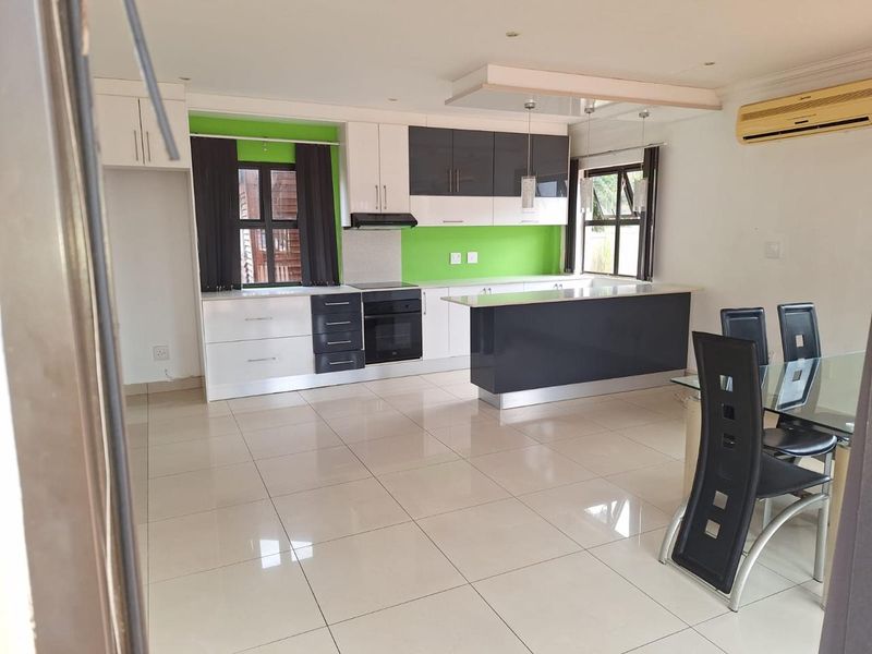 Modern open-plan kitchen and dining area featuring high-gloss cabinetry, a central island, tiled flooring, and integrated appliances.